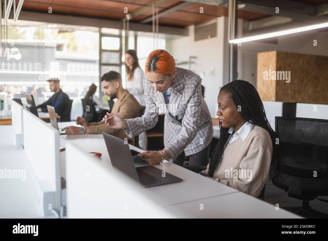Multiethnic female coworkers discussing project at table while reading documents in modern workplace Stock Photo