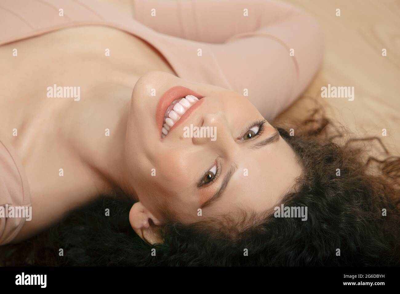 From above of tender female in beige bodysuit lying on wooden floor and looking at camera Stock Photo