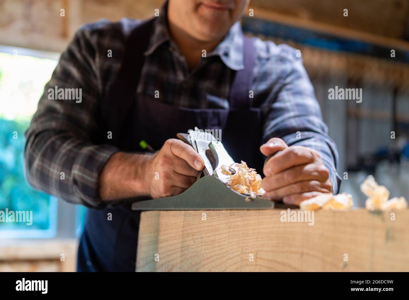 Unrecognizable male woodworker smoothing wooden detail with jack plane while working in professional carpentry workshop Stock Photo