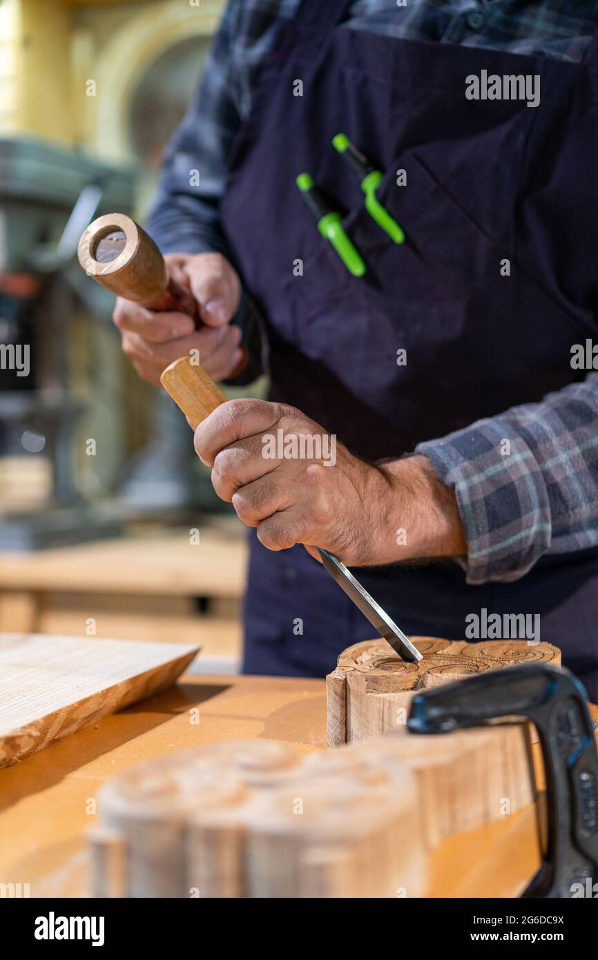 Unrecognizable male woodworker with wooden hammer and chisel carving ...