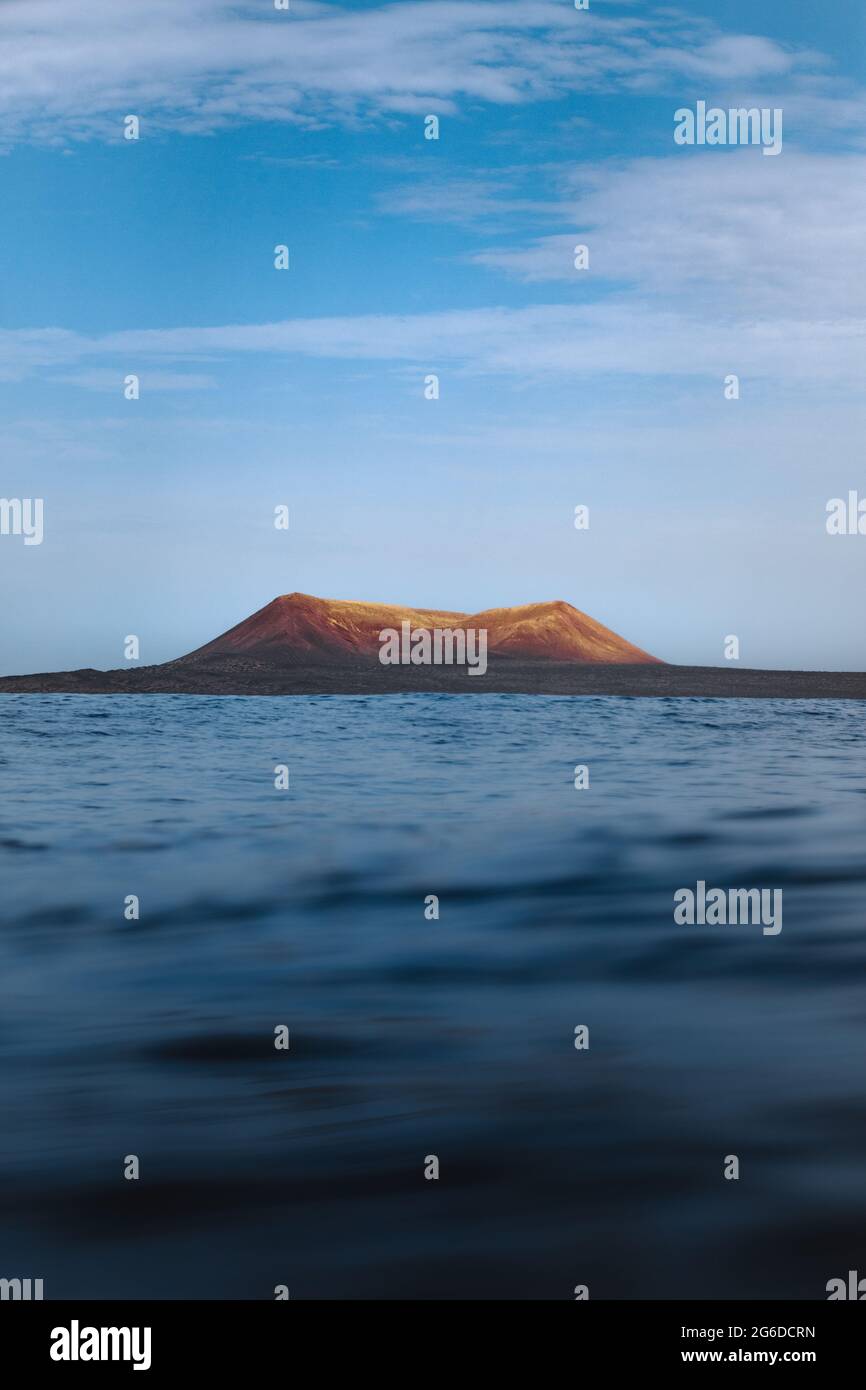 Waving blue sea rolling over seashore near distant mountain Stock Photo