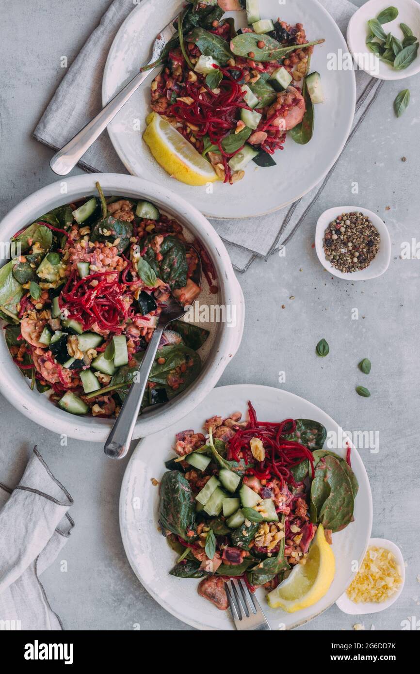 Top view of plates and bowl with yummy lentil salad with cucumbers and spinach placed near napkins on gray table Stock Photo