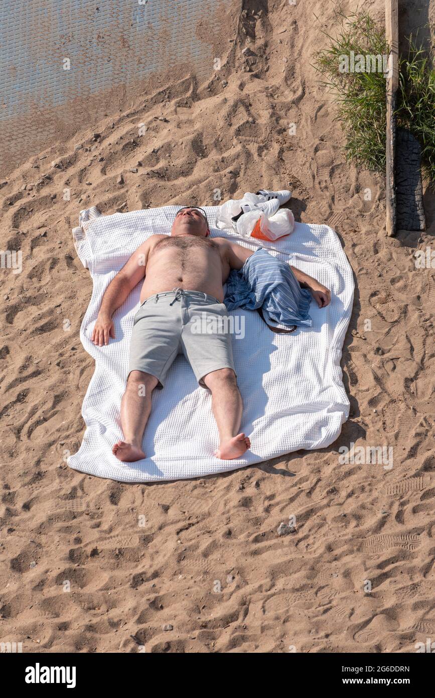 Saint Petersburg, Russia - June 20, 2021: a man sunbathes lying on a towel at the beach of Park of the 300th Anniversary of Saint Petersburg. Stock Photo