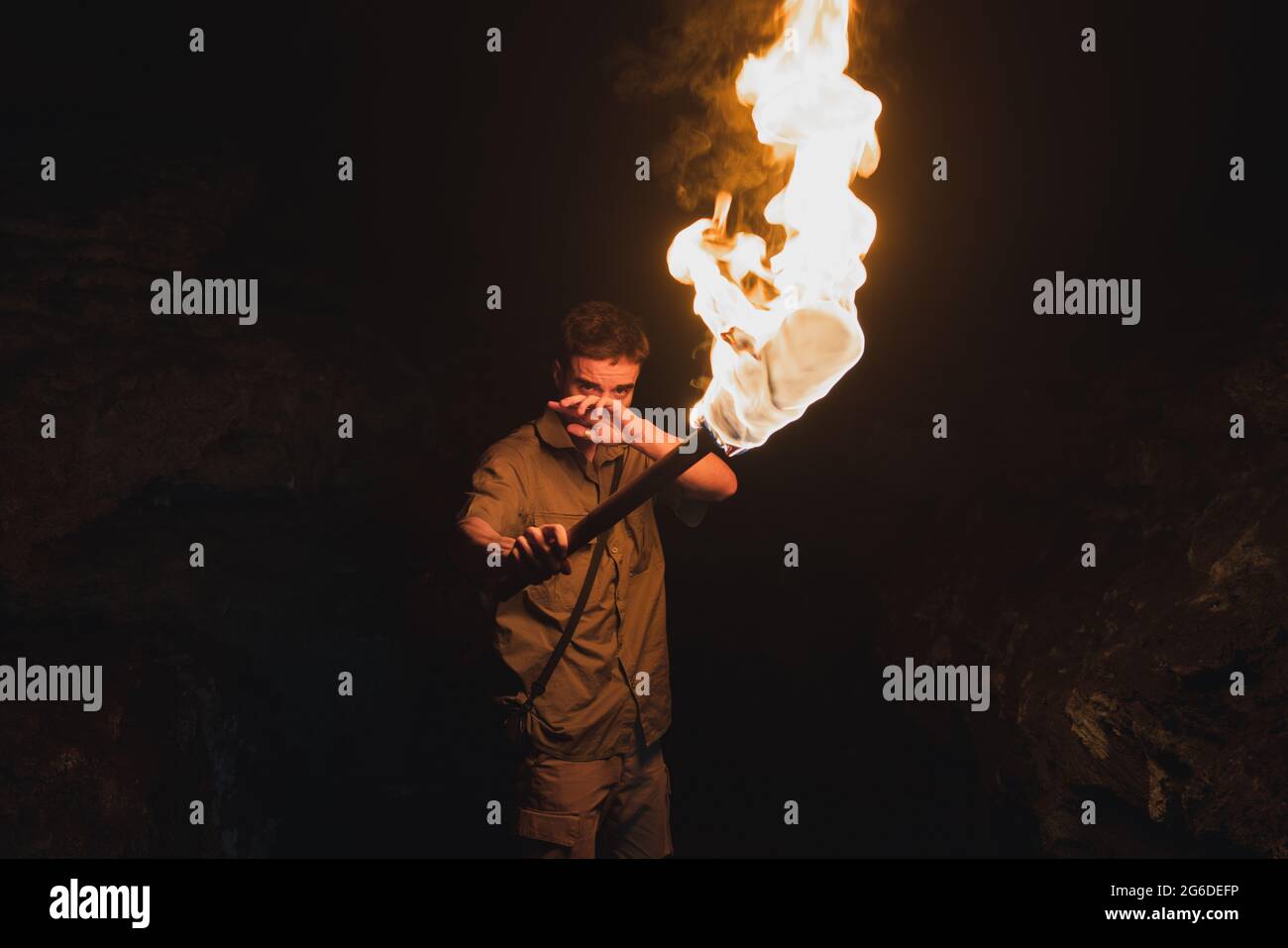 Young male speleologist with flaming torch standing in dark narrow rocky cave while exploring subterranean environment Stock Photo