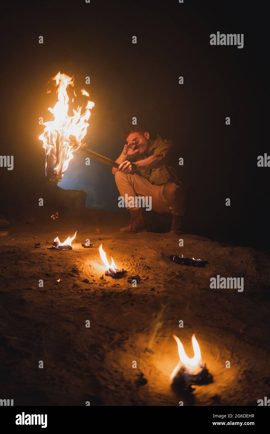 Unrecognizable male adventurer with bright burning torch crouching while exploring dark underground cave during speleology expedition Stock Photo