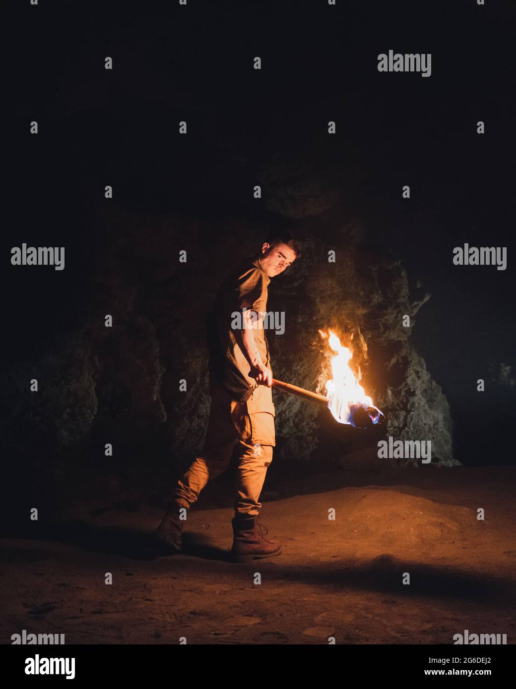 Side view of young male speleologist with flaming torch standing in dark narrow rocky cave while exploring subterranean environment Stock Photo