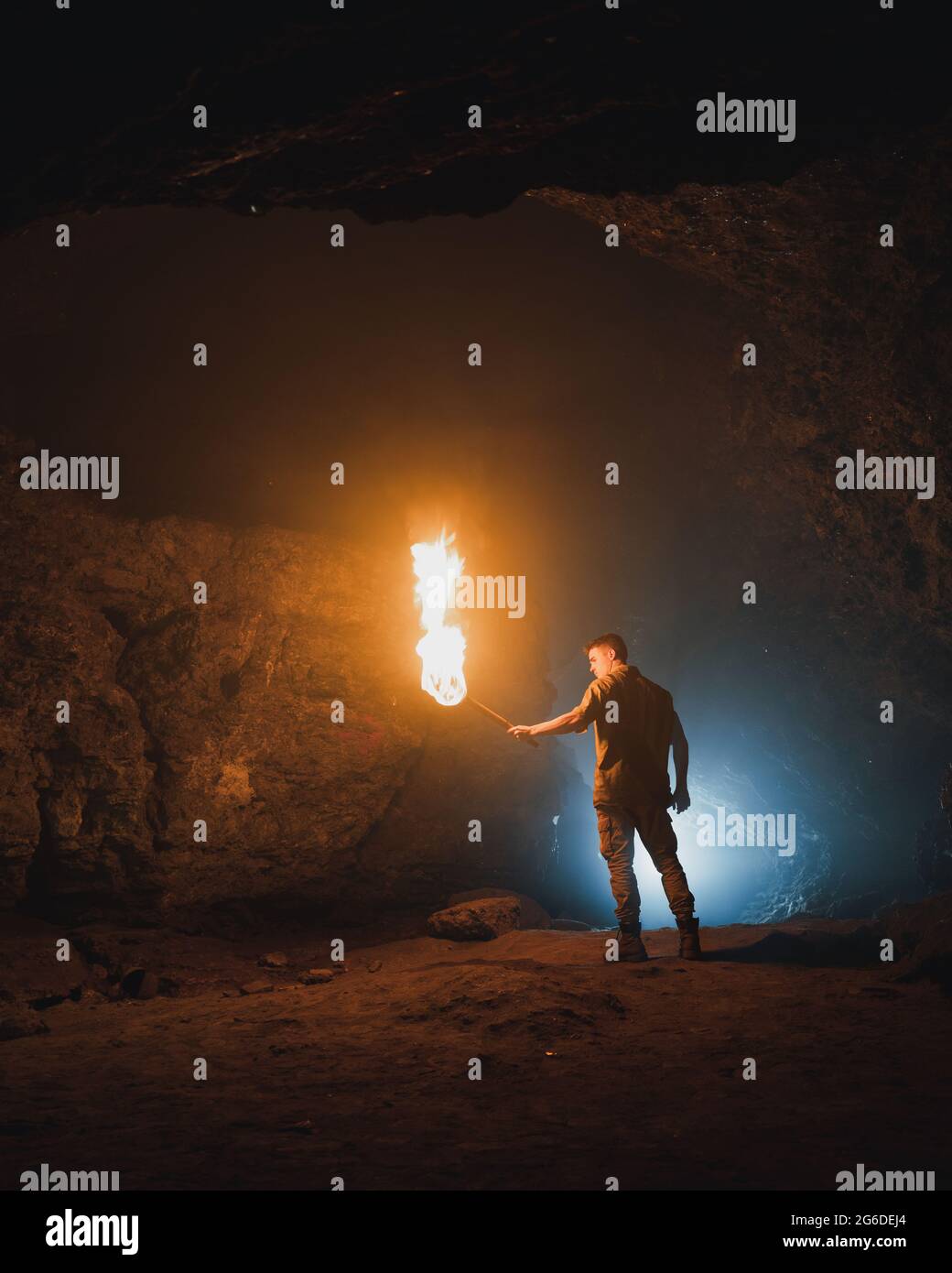 back view of young male speleologist with flaming torch standing in dark narrow rocky cave while exploring subterranean environment Stock Photo