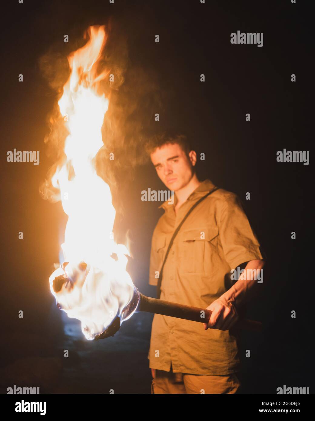 Side view of young male speleologist with flaming torch standing in dark narrow rocky cave while exploring subterranean environment Stock Photo