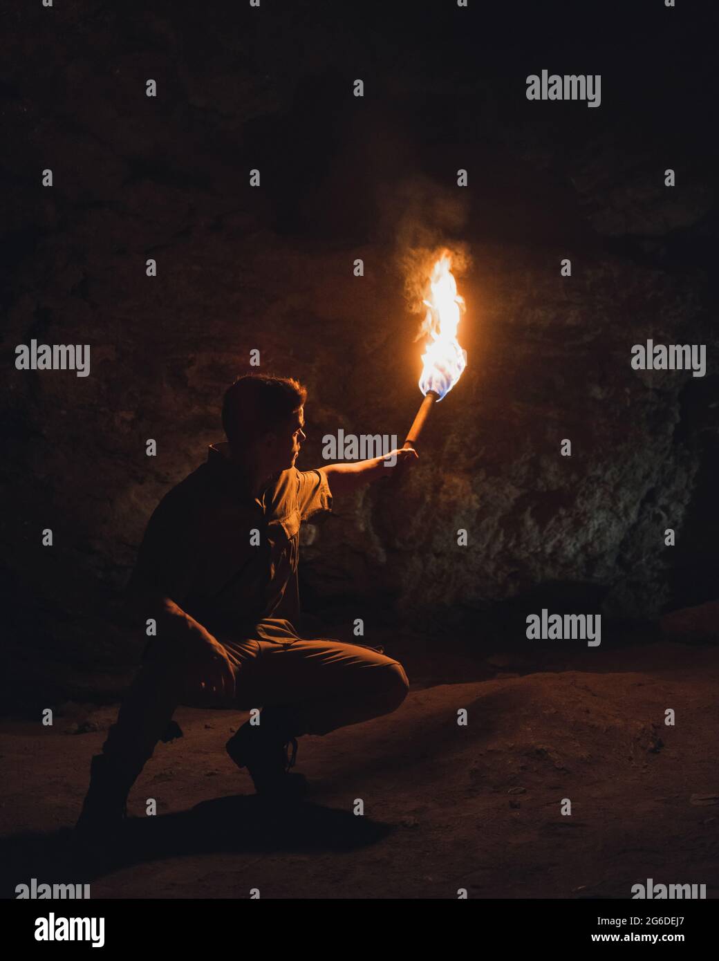 Unrecognizable male adventurer with bright burning torch crouching while exploring dark underground cave during speleology expedition Stock Photo