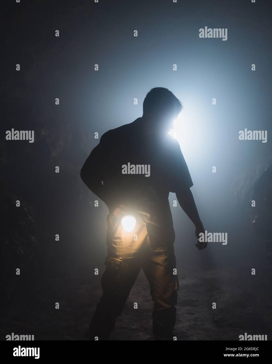 Unrecognizable male speleologist with bright flashlight in hand exploring dark subterranean cave during extremal adventure Stock Photo