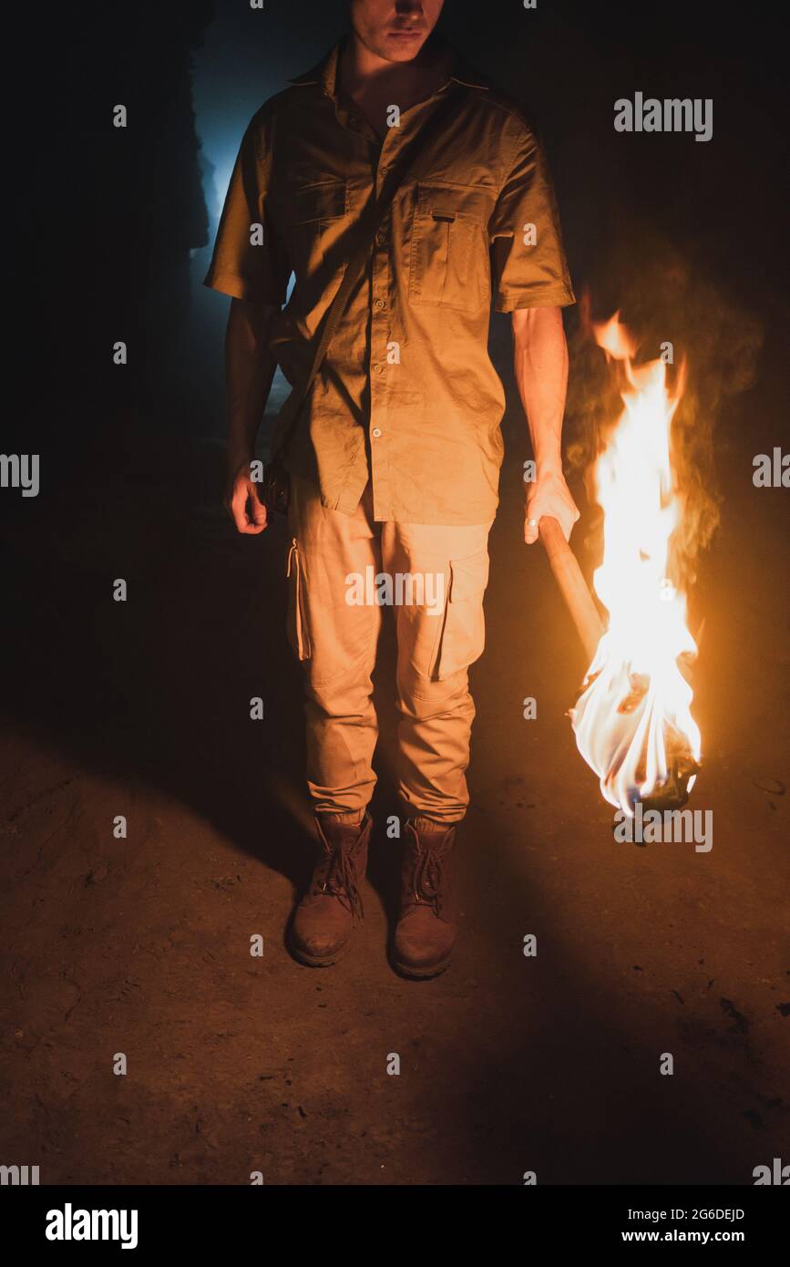 Cropped anonymous male speleologist with flaming torch standing in dark narrow rocky cave while exploring subterranean environment Stock Photo