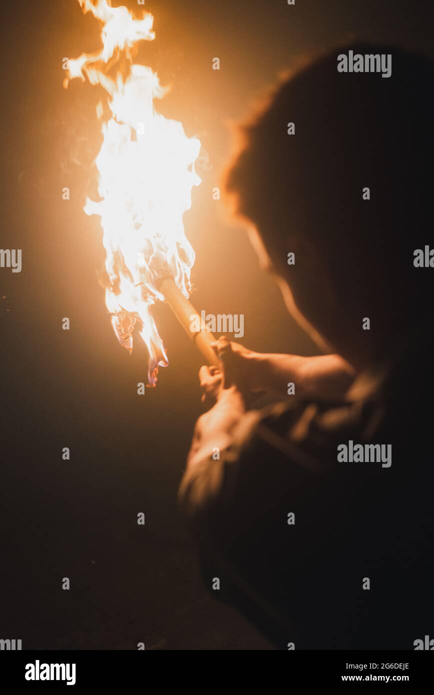 Back view of cropped anonymous male speleologist with flaming torch standing in dark narrow rocky cave while exploring subterranean environment Stock Photo