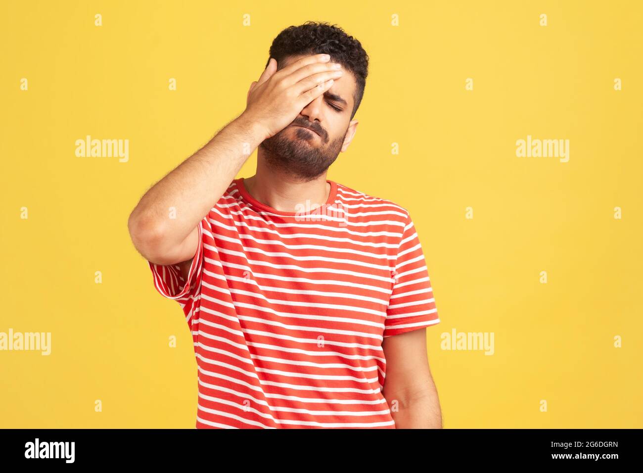 Unhappy forgetful man with beard in striped t-shirt making facepalm gesture keeping hand on head, blaming himself for bad memory, unforgivable mistake Stock Photo