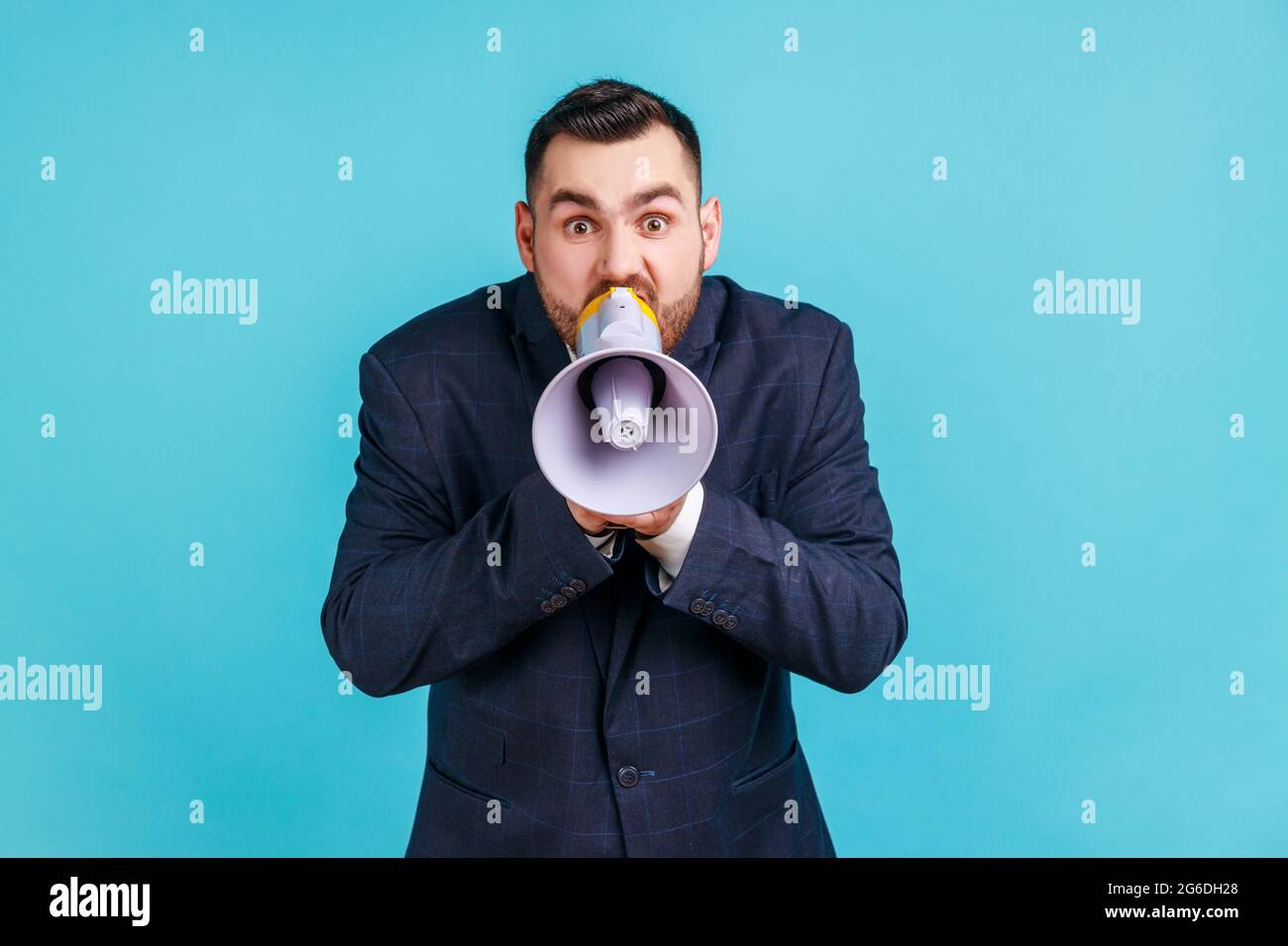 Portrait of angry nervous bearded man wearing elegant suit loudly screaming at megaphone, making announce, protesting, wants to be heard. Indoor studi Stock Photo