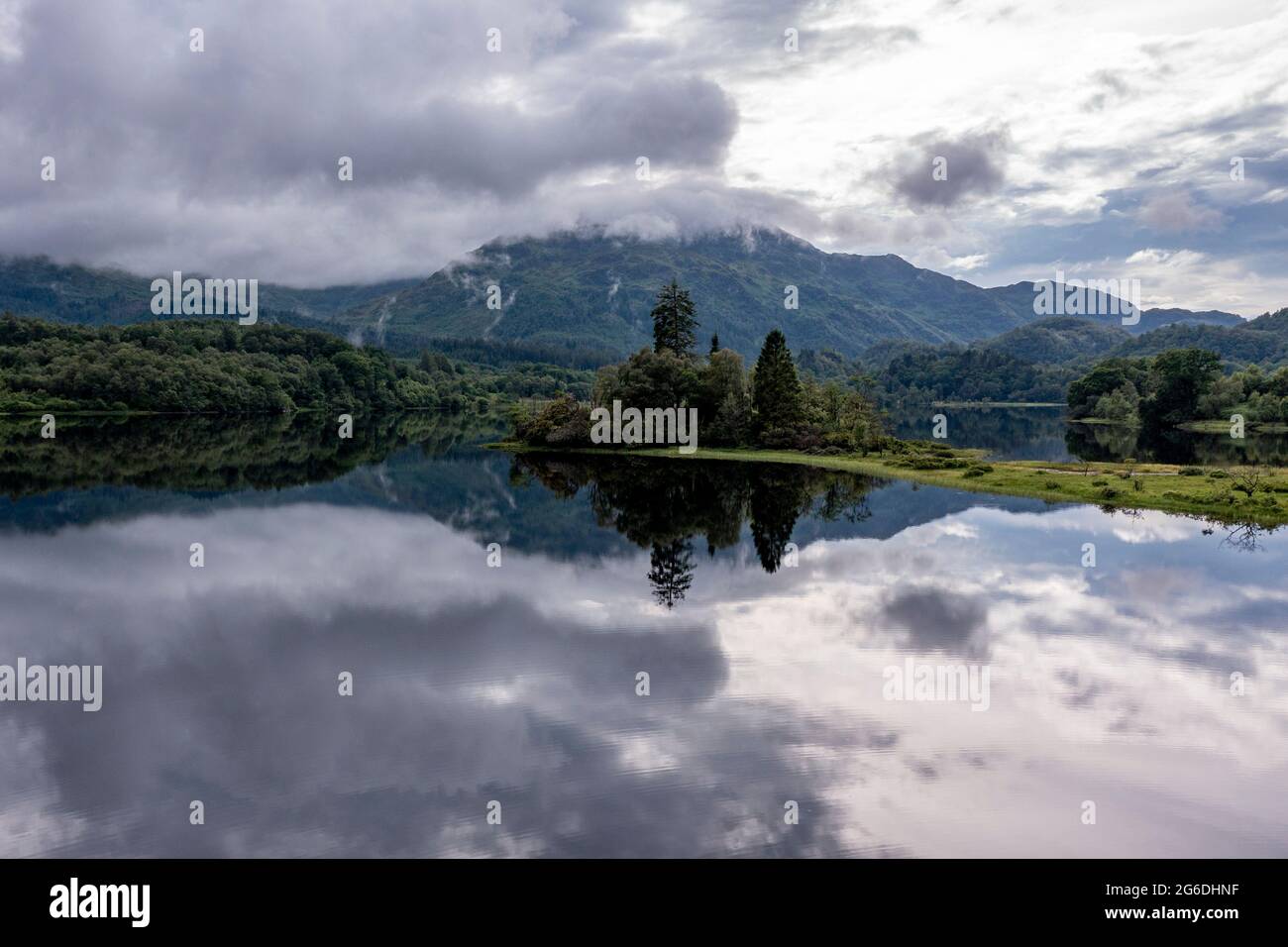 Loch Achray, Loch Lomond and Trossachs National Park, Scotland, UK. 4 July 2021. Pictured: Loch Achray turns into a mirror reflection the areas outstanding natural beauty with the Loch Achray hotel in the background at the foot of the mountains.  Credit: Colin Fisher/Alamy Live News Stock Photo