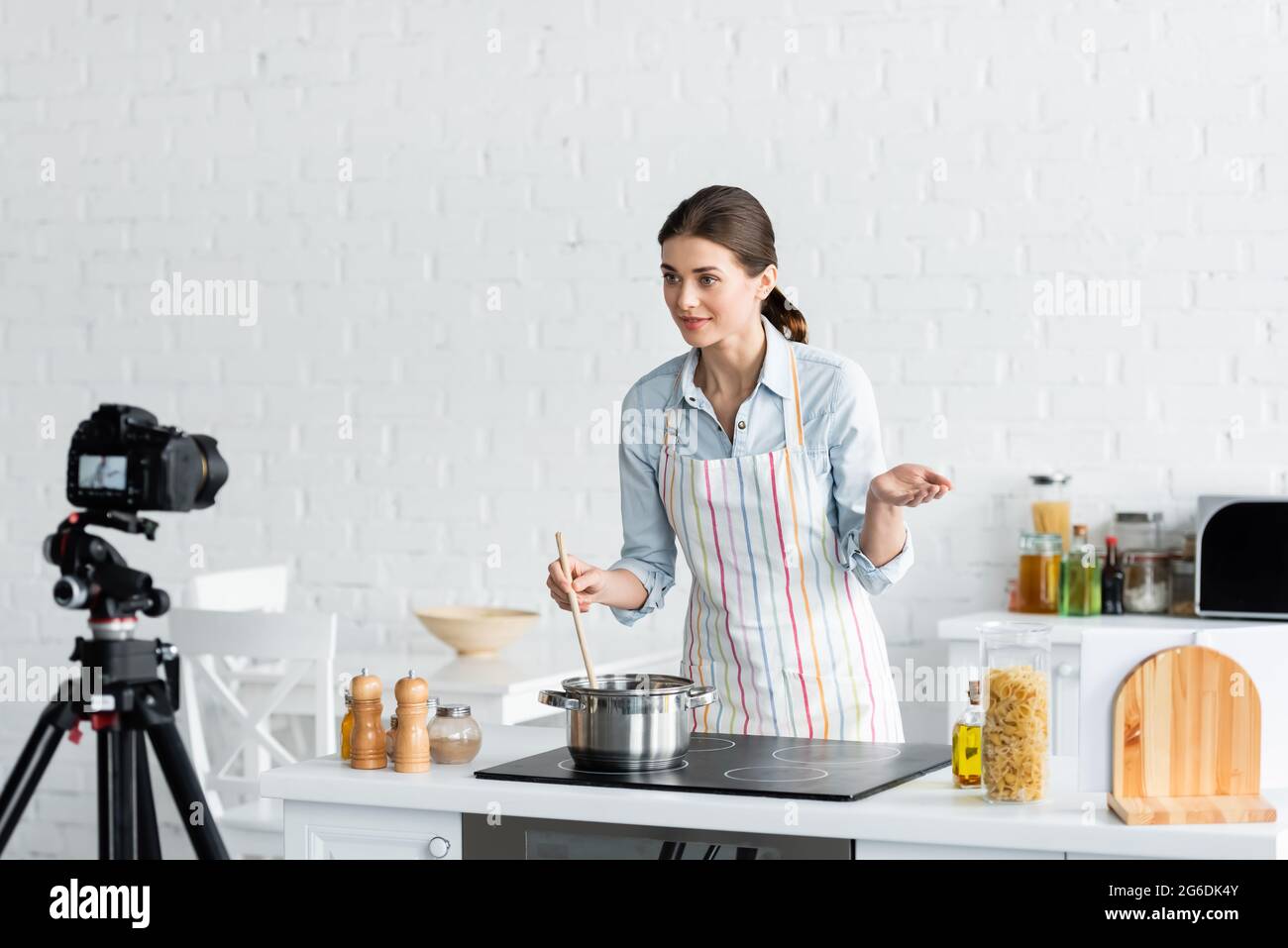 young culinary blogger talking near digital camera while preparing food in kitchen Stock Photo