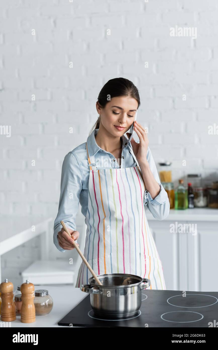 pretty housewife talking on mobile phone while preparing food in kitchen Stock Photo