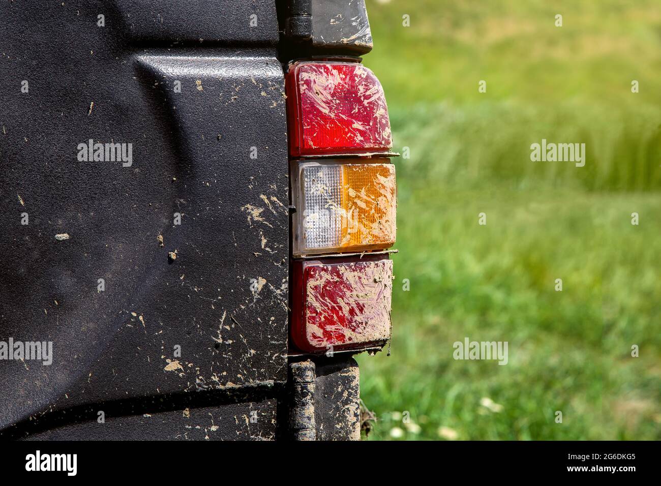 stop signal taillight with turn signals smeared with swamp close-up, dirty car rear view on the trunk lid in the background green grass in defocus. Stock Photo