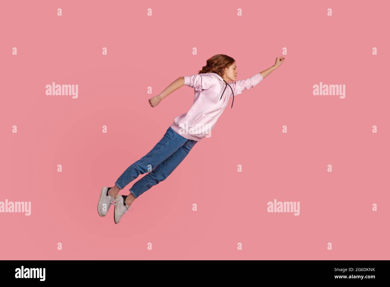 Full length portrait of motivated young female in hoodie and jeans flying in air like hero and feeling superpower, achieving goals. Indoor studio shot Stock Photo