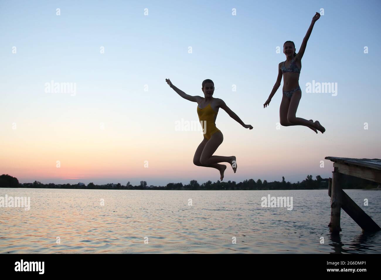 two teenage girls jump in the evening from the pier into the water Stock Photo Alamy