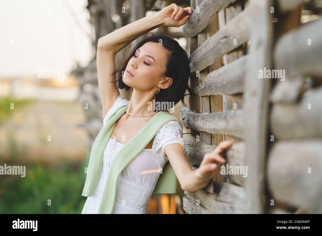 Asian woman, posing near a tobacco drying shed, wearing a white dress and green wellies. Stock Photo