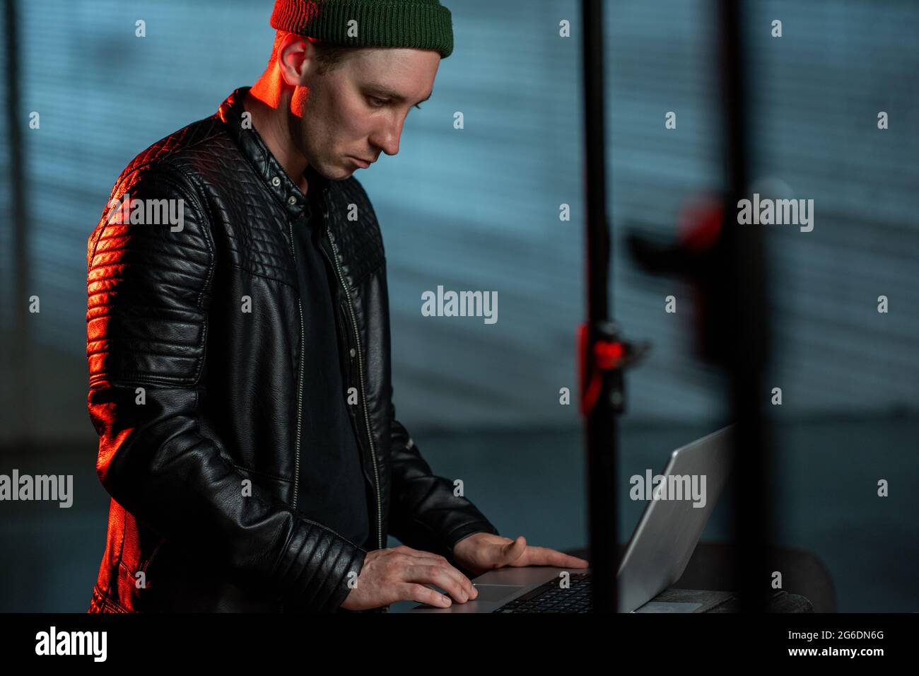 Contemporary hacker in black leather jacket using laptop Stock Photo