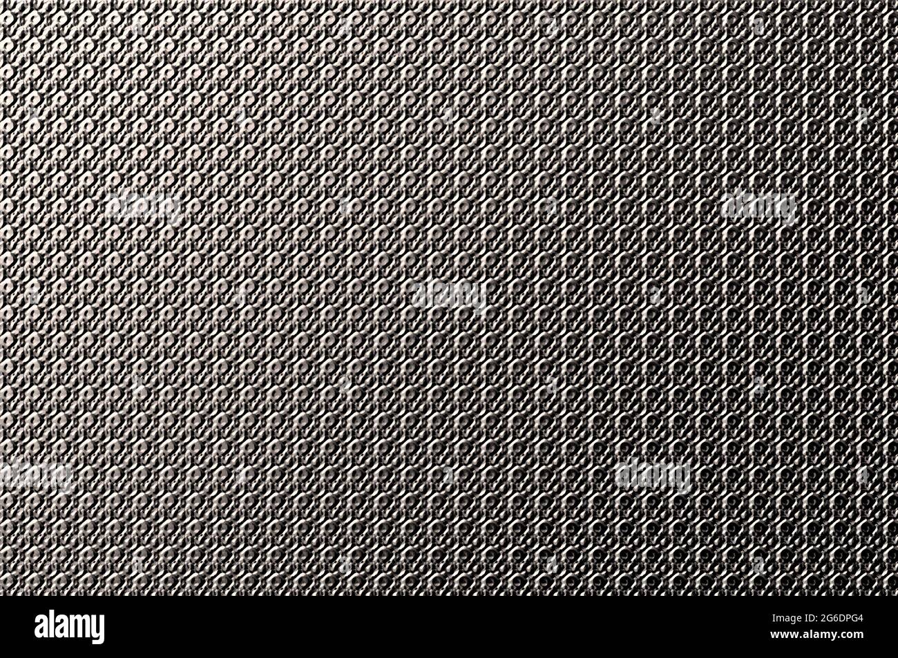 Abstract image of metal plate indented with rows of circles.  Light shines one one end and the other is darker.  Tones of grey and black. Stock Photo