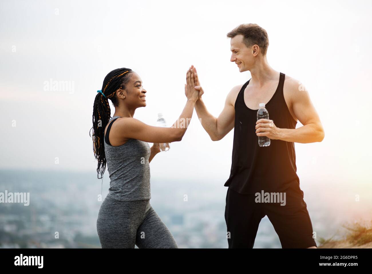 https://c8.alamy.com/comp/2G6DPR5/smiling-young-couple-dressed-in-sport-clothes-giving-high-five-to-each-other-after-active-workout-on-fresh-air-african-woman-and-caucasian-man-holding-bottle-of-fresh-water-2G6DPR5.jpg