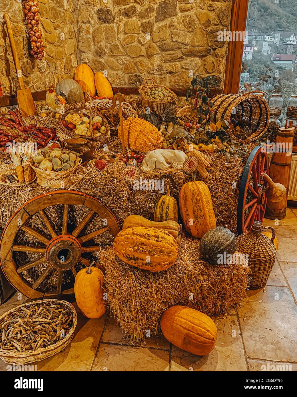 Pumpkins, corn, peas, onions, apples, pears, bell peppers, a basket full of fruit in the hay with a wheelchair wheel on a stone wall Stock Photo