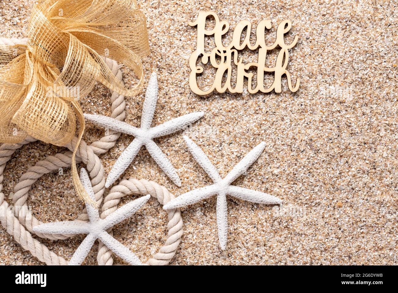 beach or tropical theme holiday greeting with white starfish, nautical rope, mesh net bow and Peace on Earth on beach sand all in natural tones Stock Photo
