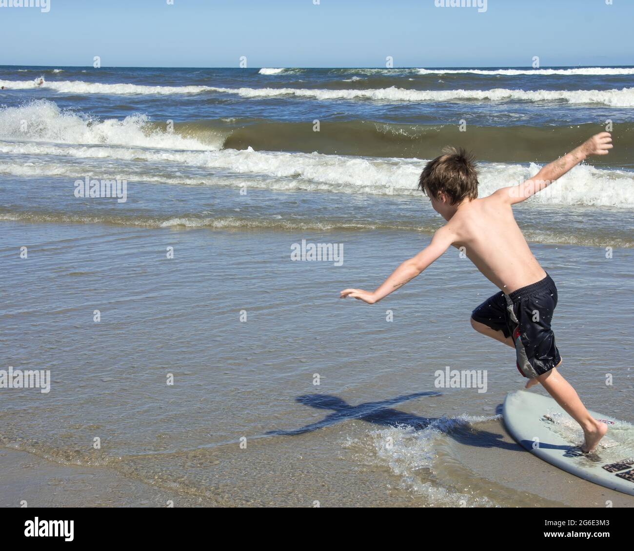 Young boy on a boogie board balancing himself with his arms, at the edge of the ocean during summer. Stock Photo