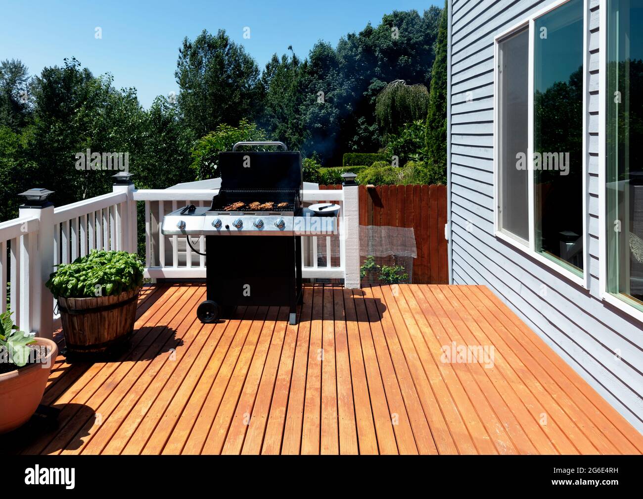 Outdoor BBQ cooker with lid open displaying smoke coming out while on home wooden deck during summertime Stock Photo