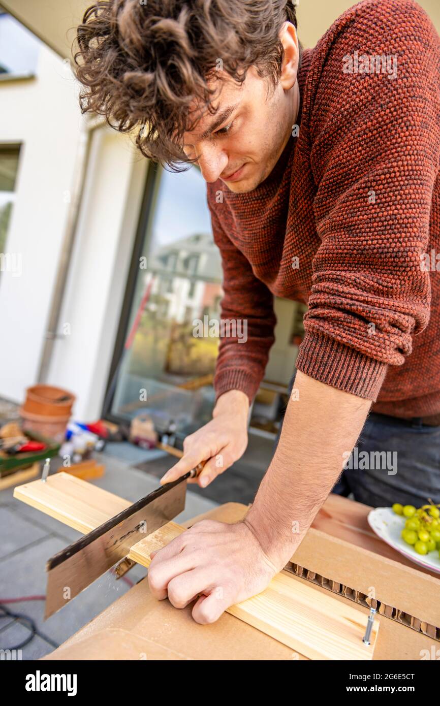 Young man doing DIY in his apartment, sawing board with a handsaw Stock Photo