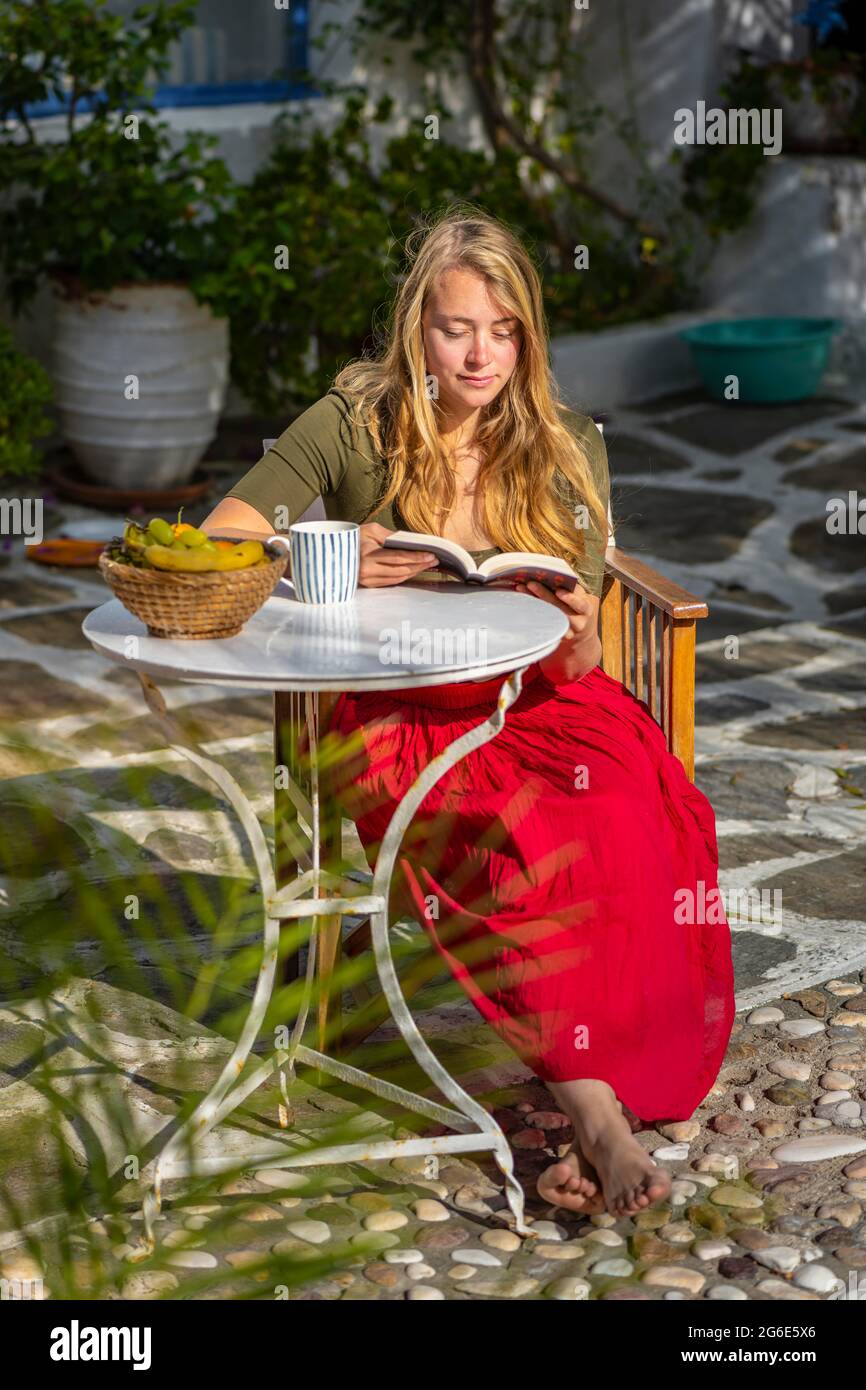 Young woman reading, breakfast on holiday, courtyard, Greece Stock Photo