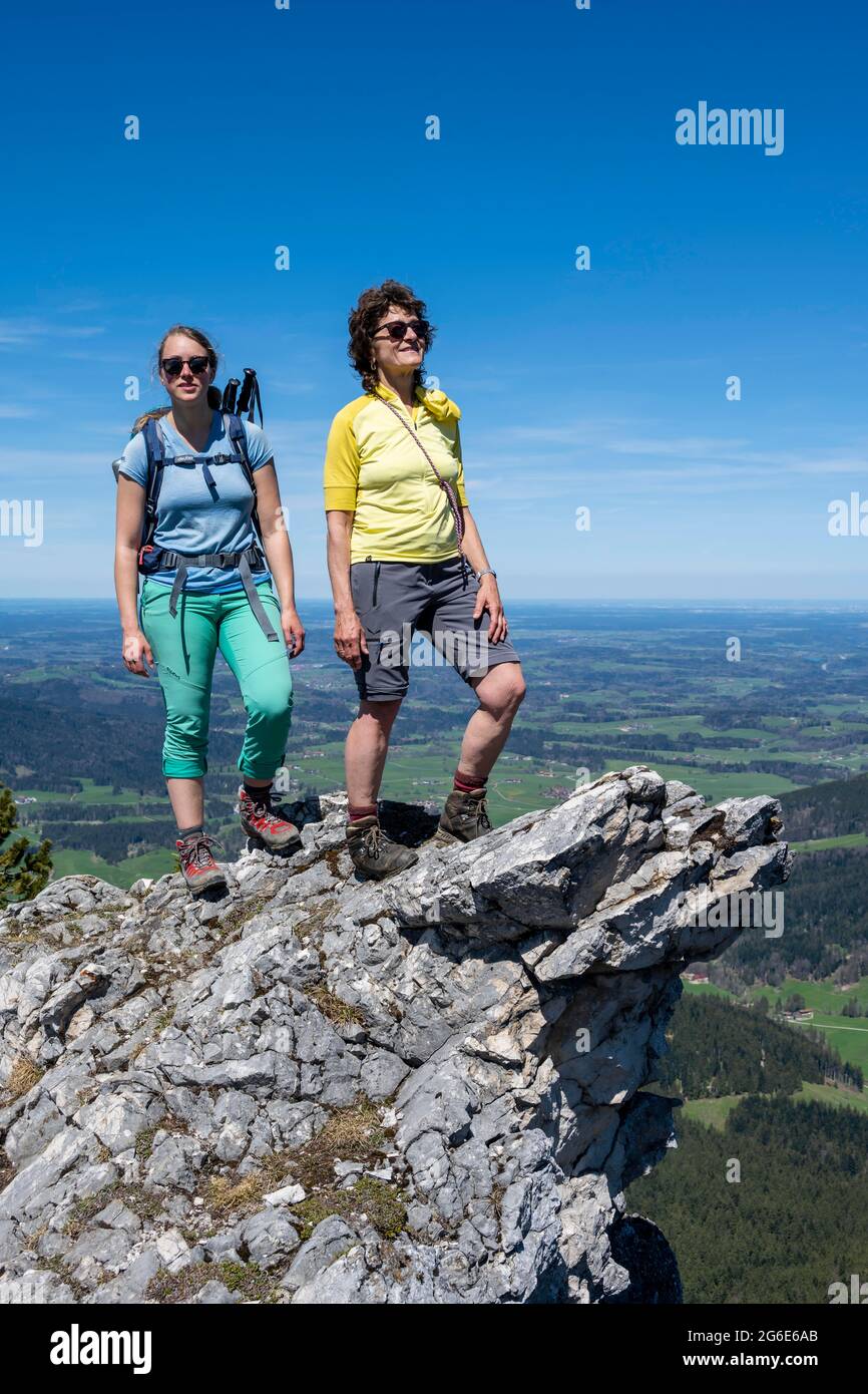 Two female hikers looking over the alpine foothills, on the summit of Breitenstein, Fischbachau, Bavaria, Germany Stock Photo