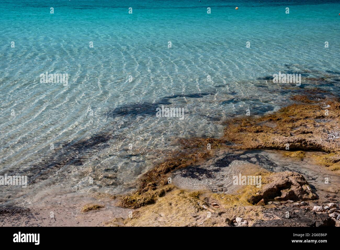 Calm sea surface, small ripples on rough shore, shallow water. Turquoise blue color water, sandy seabed and rocky coast, Summer holidays at a paradise Stock Photo