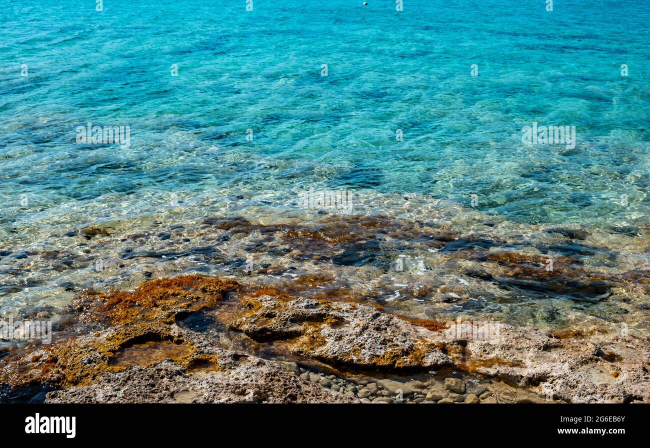 Sea water turquoise blue color and rocky coast, Calm surface, small ripples on rough shore, shallow water. Summer holidays at a paradise island. Cycla Stock Photo