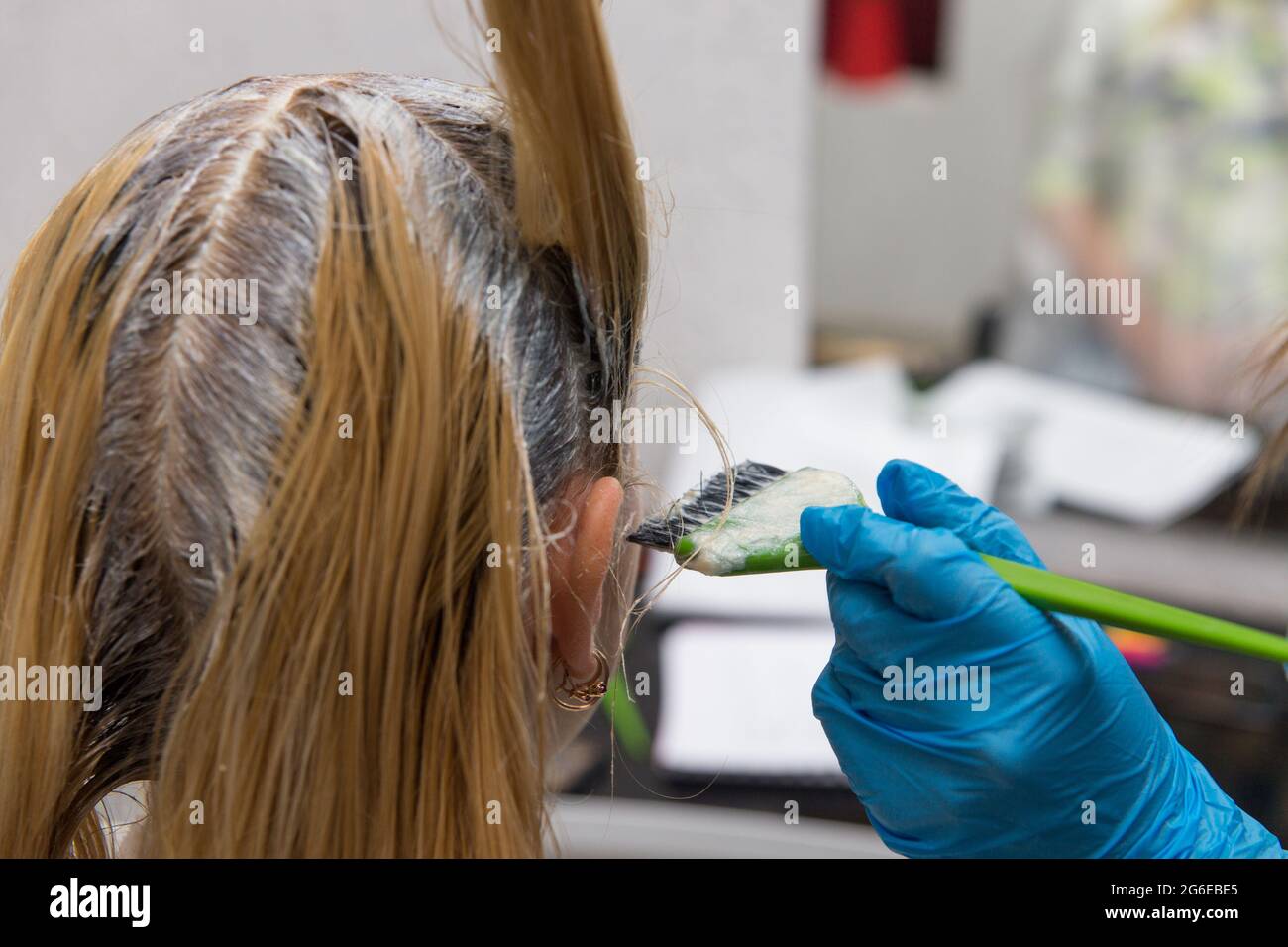 A hairdresser applies paint with a brush to a woman's hair in a beauty salon.. Hair colouring in