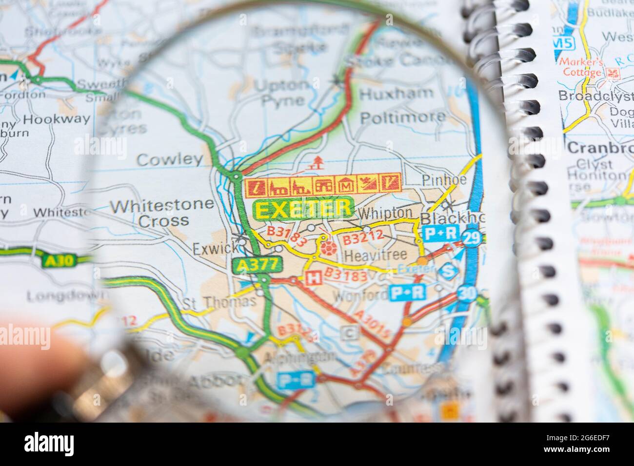 Closeup of a page in a printed road map atlas with a man's hand holding a magnifying glass showing an enlargement of the city of in Exeter, England Stock Photo