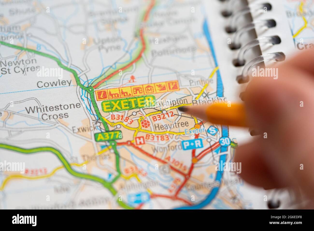 Closeup of a page in a printed road map atlas with a man's hand holding a pencil pointing at the city of Exeter in England. Concept: map reading Stock Photo