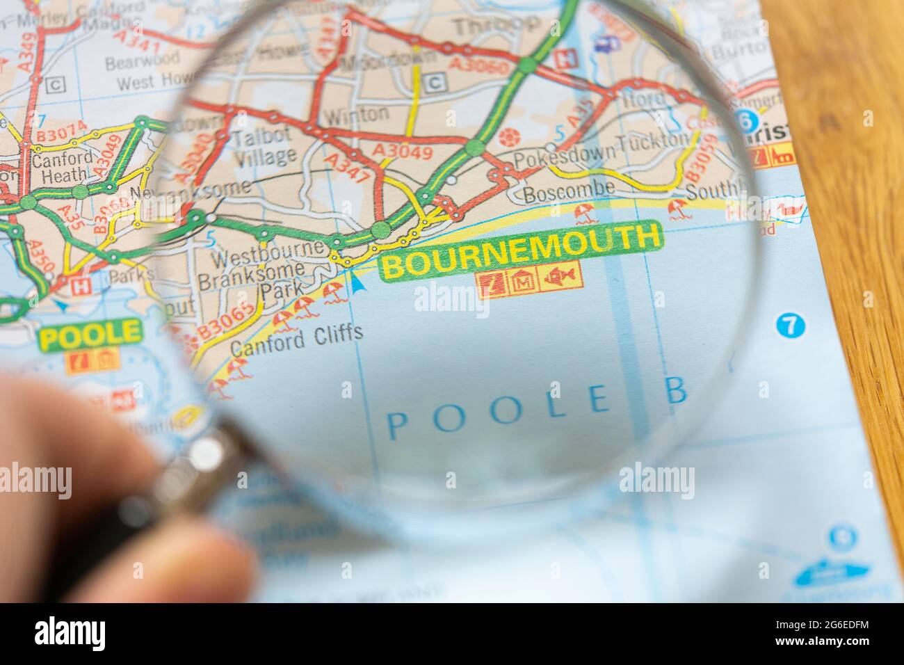 Closeup of a page in a printed road map atlas with a man's hand holding a magnifying glass showing the coastal resort town of Bournemouth in England Stock Photo