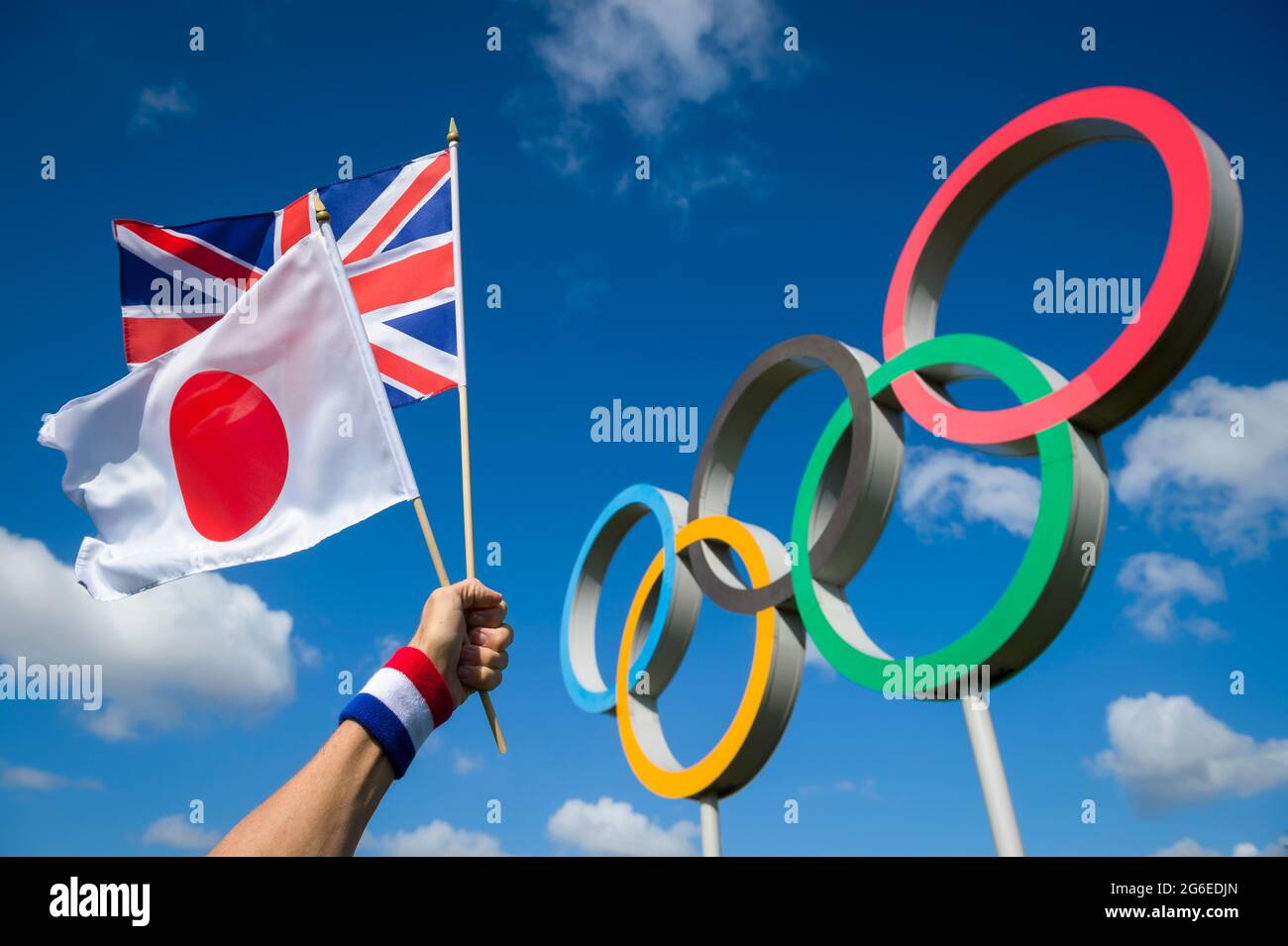 RIO DE JANEIRO - MARCH, 2016: Athlete holds Japanese and UK flags together in front of a large set of Olympic Rings under bright blue sky. Stock Photo