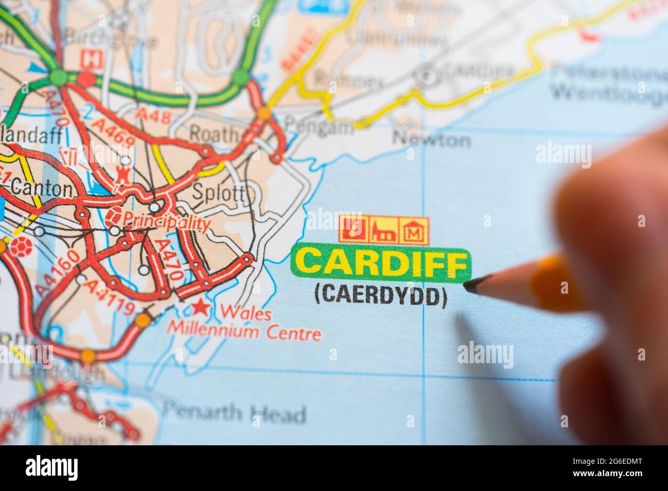 Closeup of a page in a printed road map atlas with a man's hand holding a pencil pointing at the capital city of Wales - Cardiff (Caerdydd) Stock Photo