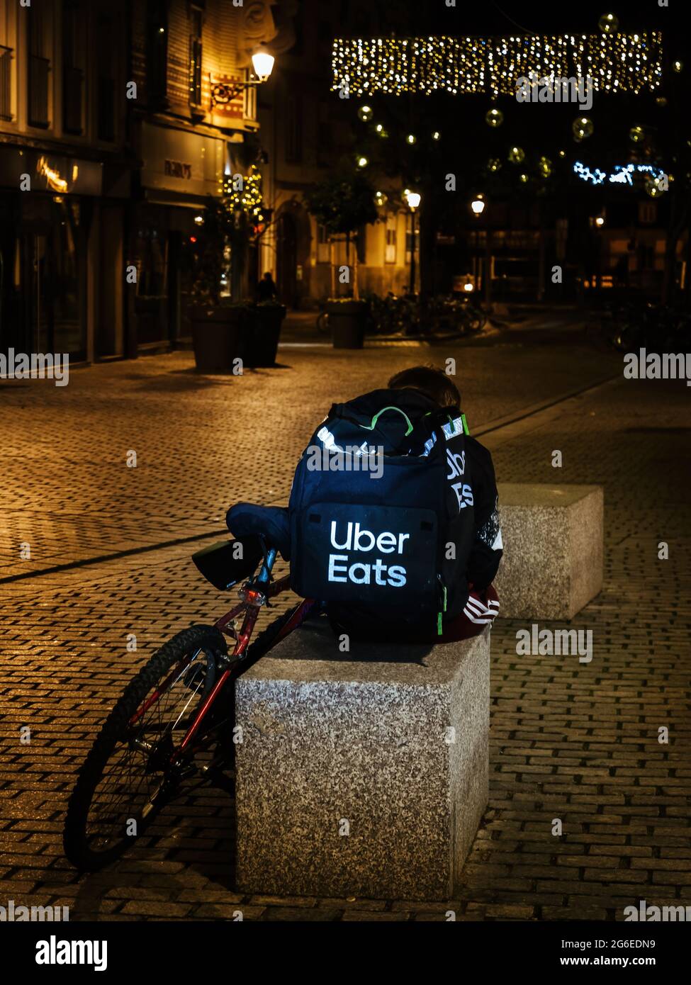 Lonely uber eats app driver delivery young man sitting on the stone
