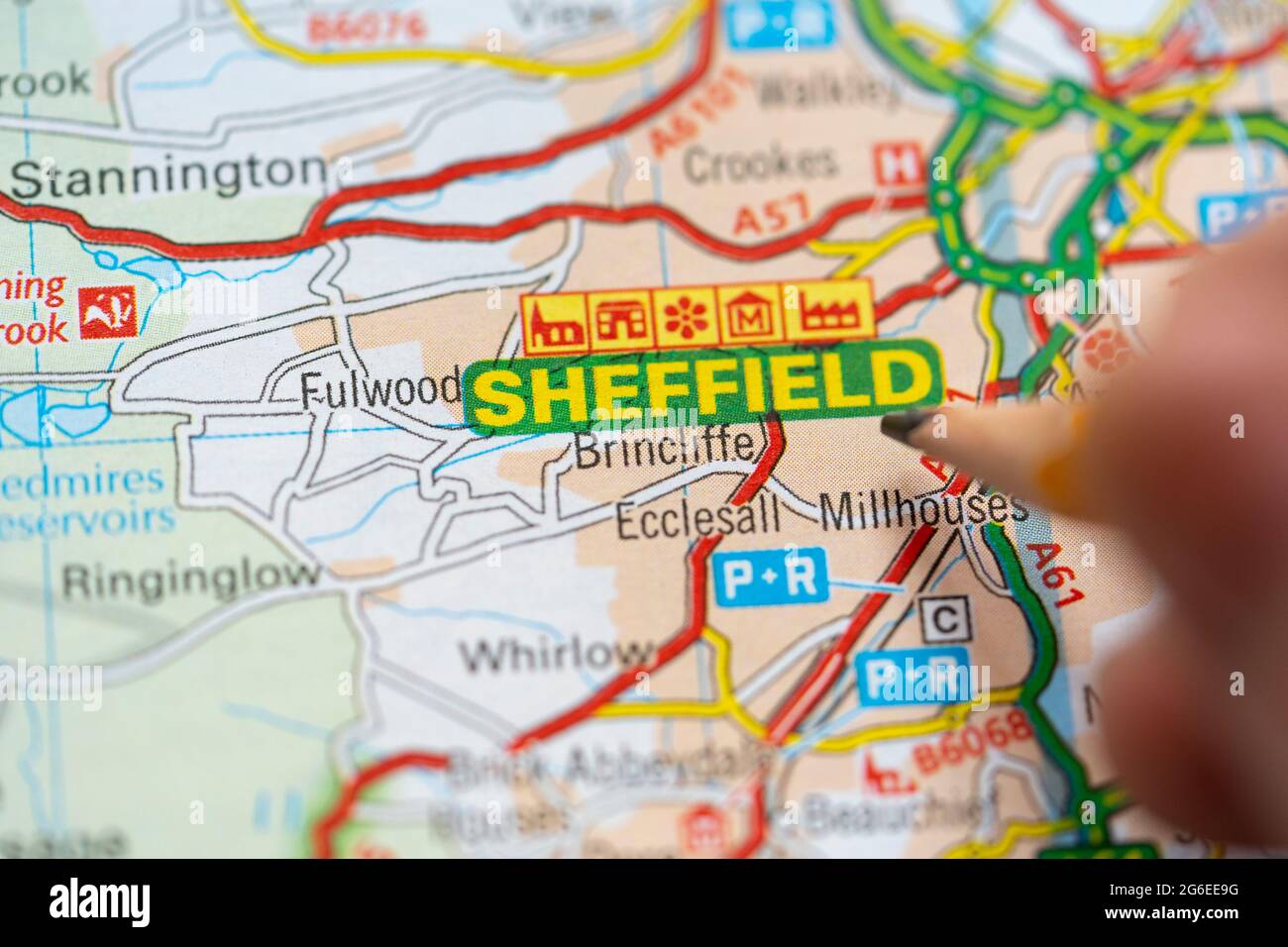 A macro closeup of a page in a printed road map atlas with a man's hand holding a pencil pointing Sheffield, England. Concept: map reading Stock Photo