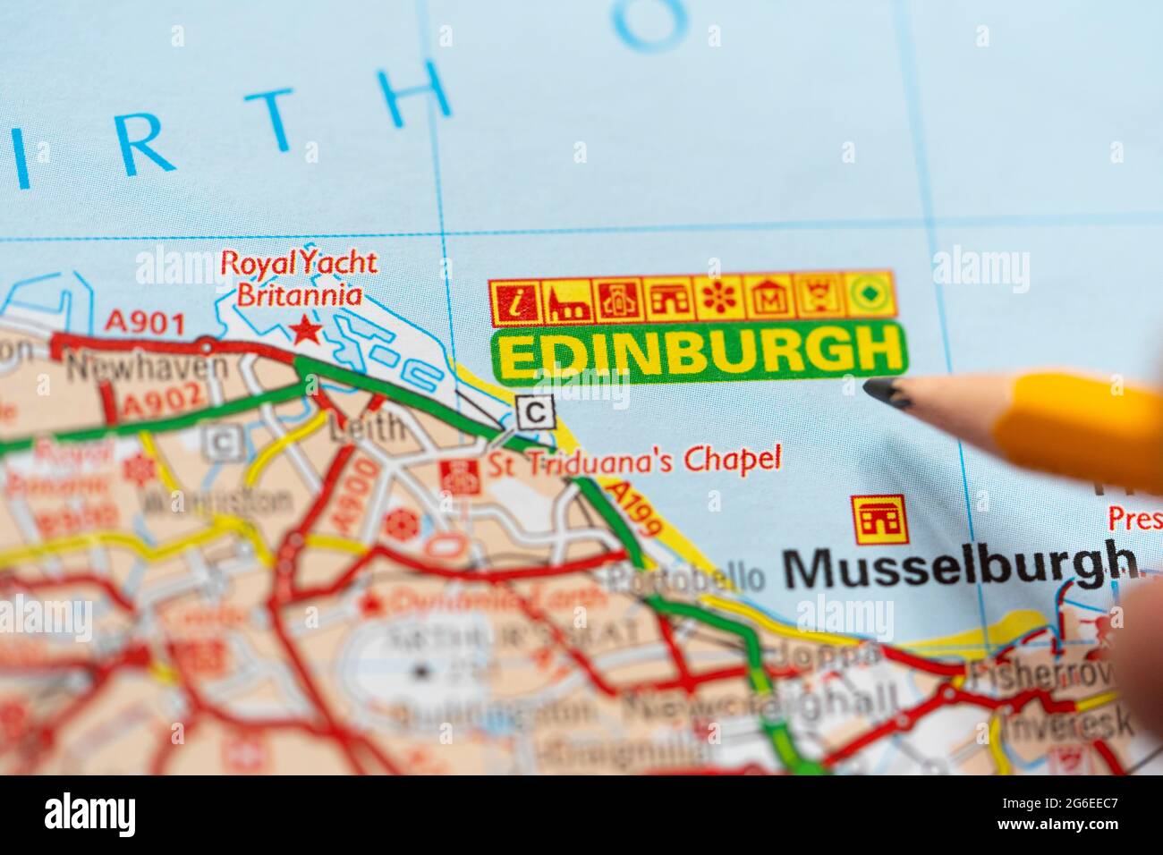 A macro closeup of a page in a printed road map atlas with a man's hand holding a pencil pointing at Scotland's capital city - Edinburgh Stock Photo