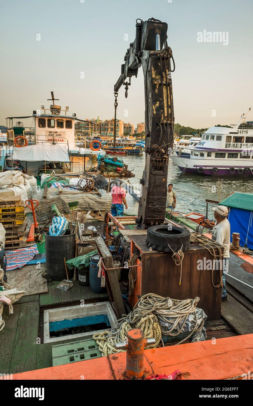 A man uses a crane to load a large diesel motor aboard a barge moored at the Sai Kung waterfront, New Territories, Hong Kong Stock Photo