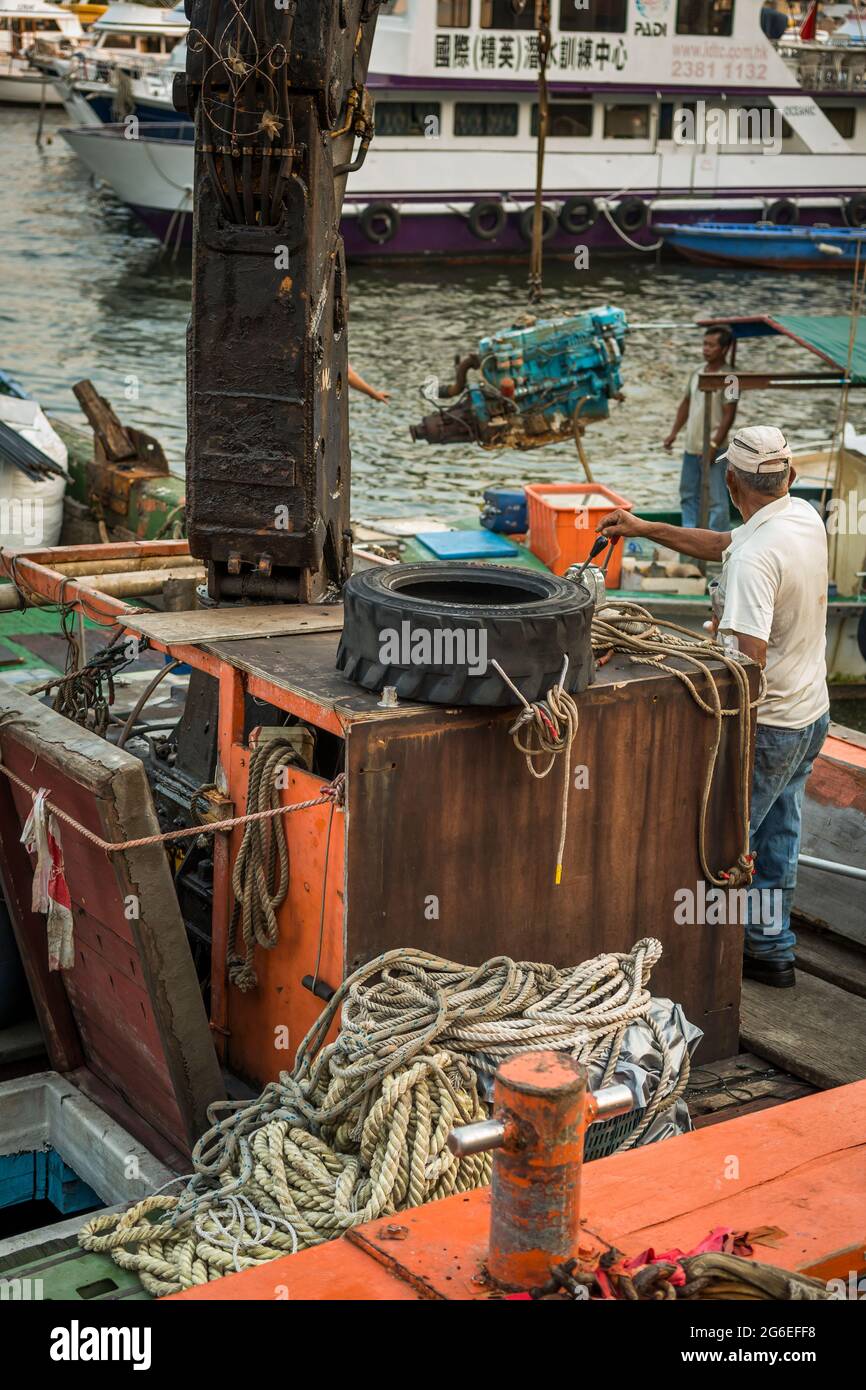 A man uses a crane to load a large diesel motor aboard a barge moored at the Sai Kung waterfront, New Territories, Hong Kong Stock Photo