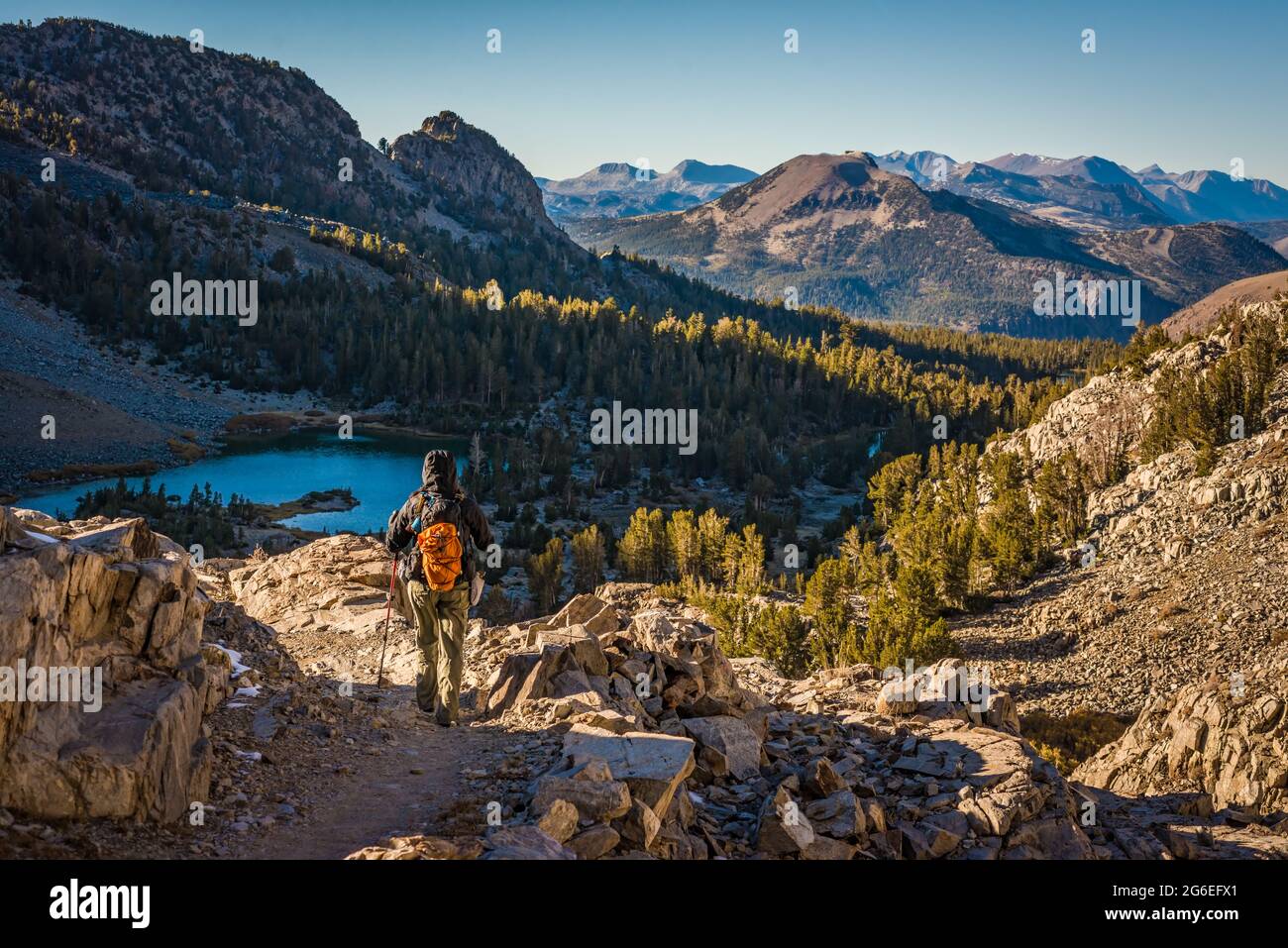 Day hiker descending the granite covered mountains in the John Muir Wilderness with Barney Lake and Mammoth Mountain in the background Stock Photo