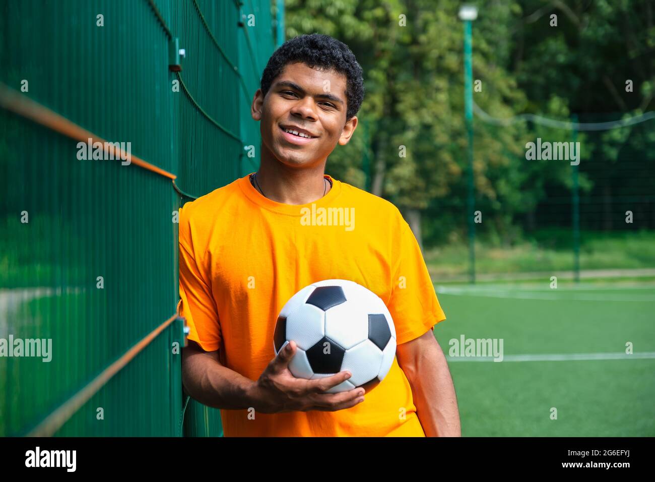 African-American man holding soccer ball while standing against fence Stock Photo